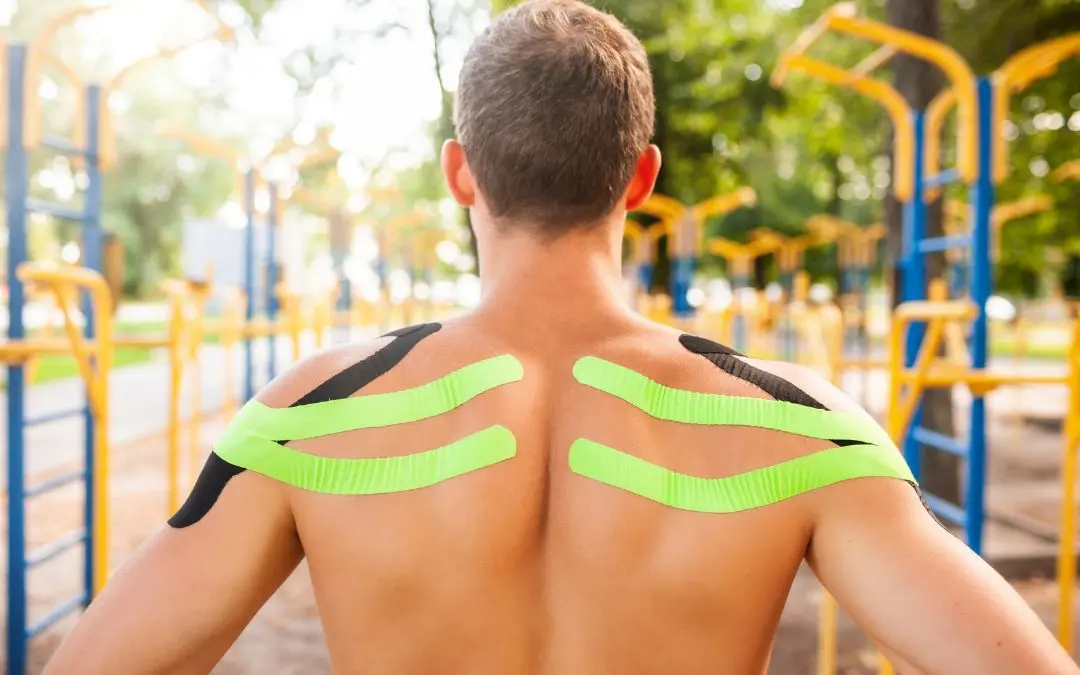 Pratiquant de street workout vu de dos, épaules couvertes de bandes de kinésiologie vertes et noires, devant des barres de parc
